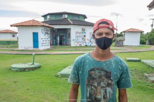 Kauan Alves em pé na frente da Estação da Juventude. Ele está de camisa verde, máscara e Boné