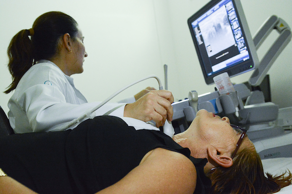 Profissional de saúde, olha para a tela do computador, onde aparece a imagem da garganta da paciente examinada em aparelho de ultrassonografia do centro de prevenção ao câncer de Boa Vista