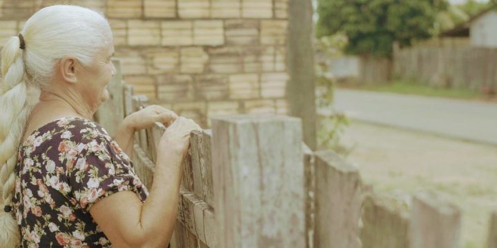 Dona Eva, dentro de casa, observa a rua asfaltada. Ela é prova do asfalto em Mucajaí