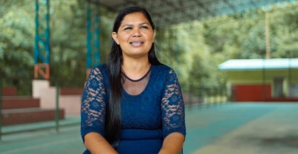 Elisângela sentada em um ginásio fala sobre saúde e bem-estar. Ela veste camisa azul