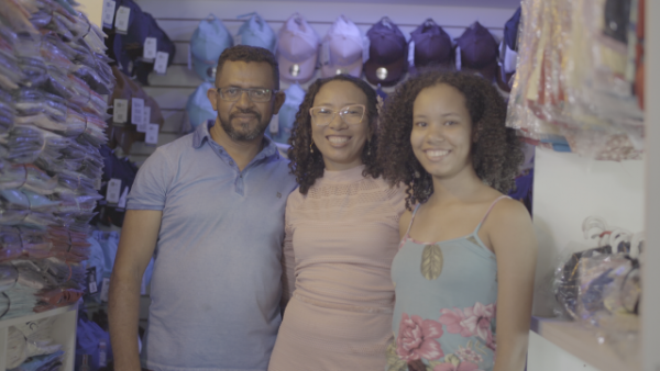 Marido de Ana Amélia, Ana Amélia e um das filhas dela. Estão felizes após Ana Amélia abrir o próprio negócio
