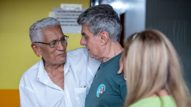 Romero Jucá e Teresa Surita olham para um homem de cabelos brancos que está sorrindo